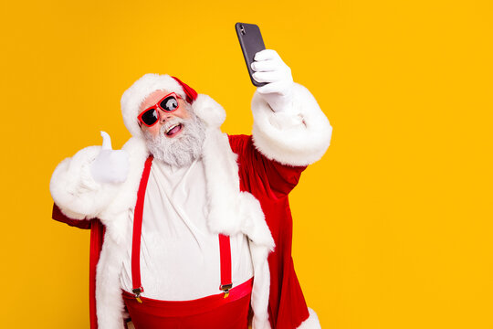 Santa Claus taking a selfie with sunglasses and thumbs up in a red suit on a bright yellow background