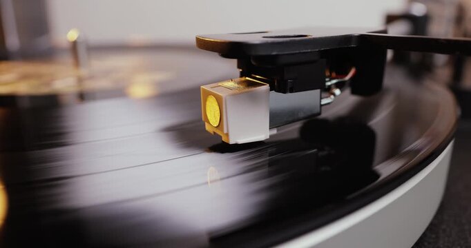 Detailed close-up of a turntable tonearm with white cartridge headshell, positioned over a black vinyl record on the platter, highlighting audio equipment precision.