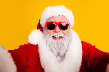 Naklejka premium Santa Claus wearing red sunglasses and a fur-trimmed suit smiling broadly in a modern festive portrait against a bright yellow background