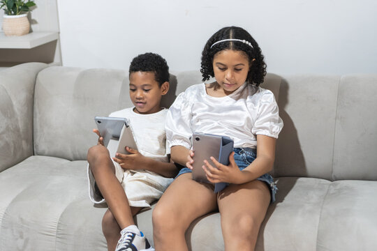 Children relaxing on couch using digital tablets