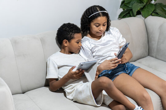 Children using digital tablets on sofa at home