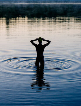 White woman standing in calm lake water at sunset creating ripples