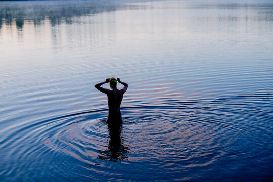 White woman standing in lake putting on swim cap with rippling water