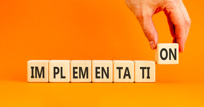 Implementation word symbol. Concept word Implementation on beautiful wooden blocks. Beautiful orange table orange background. Businessman hand. Business implementation word concept. Copy space.