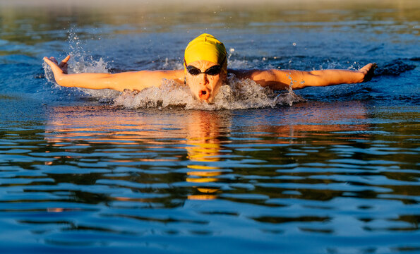 White swimmer doing butterfly stroke in open water lake at sunrise