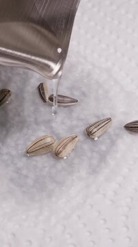 Vertical video. Water Pours Over Striped Sunflower Seeds on White Paper Towel, Close Up Seed Soaking Supports Planting Preparation and Care
