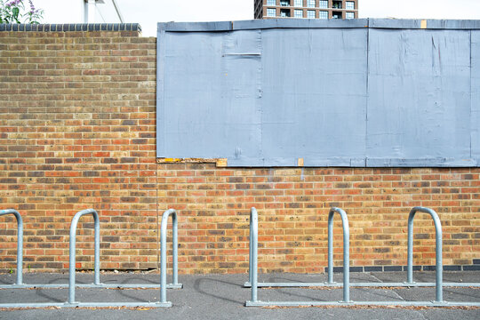 Brick wall and bicycle racks beside a boarded urban facade showing simple street infrastructure textures and everyday architectural detail