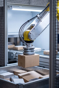 Robotic arm lifting a cardboard box with a suction gripper