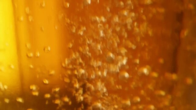 Carbonated beverage bubbles rise through amber liquid in a transparent glass macro close-up. Beverage advertising, soft drink promotion, and food and beverage campaigns.