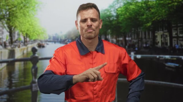 Man in orange uniform points finger toward viewer in a studio with a canal backdrop, gesturing instruction and emphasis; safety warning.