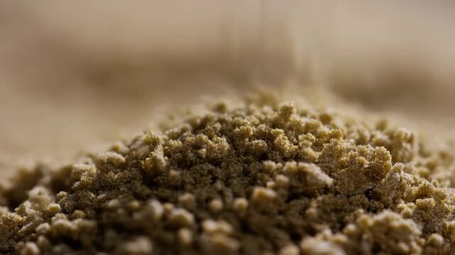 Granular material falls onto a powder mound in a shallow-focus macro close-up. Industrial process presentations, materials science education, and manufacturing advertising.