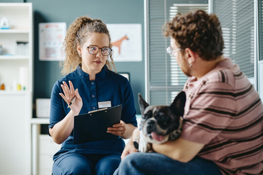 Young adult Caucasian female veterinarian consulting young adult Caucasian male pet owner with dog in clinic. Scene useful for veterinary services and pet care marketing