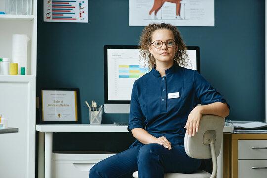 Portrait of young adult Caucasian woman veterinarian sitting near computer in veterinary clinic. Visual ideal for pet healthcare advertising and medicine campaigns