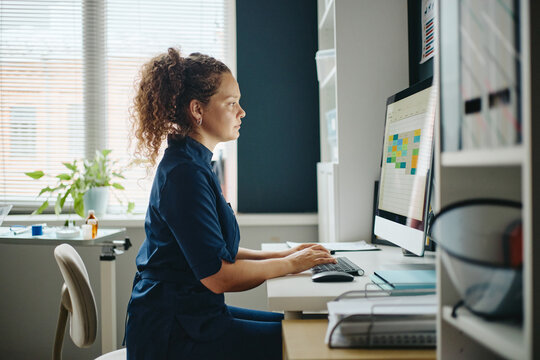 Young adult Caucasian female doctor working on computer at vet clinic desk, managing appointment schedule. Visual useful for healthcare software and clinic management promotion