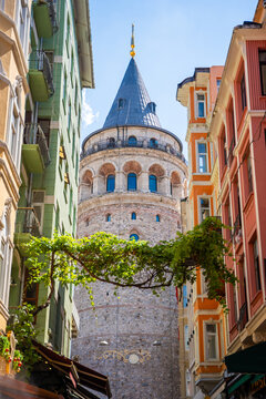Galata Tower visible between colorful buildings in Istanbul, Turkey, with clear blue sky and decorative lights hanging above the street