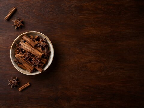 Rustic cinnamon sticks and star anise in ceramic bowl, aromatic winter spices on dark wooden background, culinary food photography with copy space