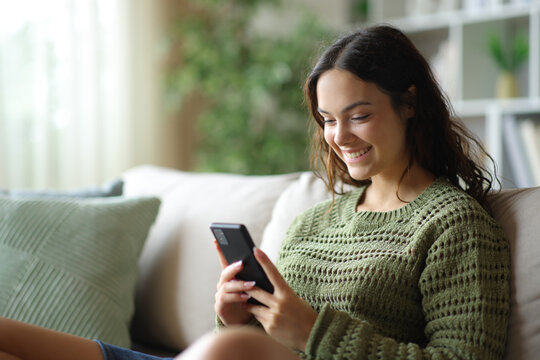 Happy young woman using smart phone on a sofa
