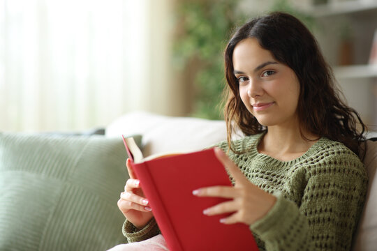 Satisfied young reader holding book looking at you