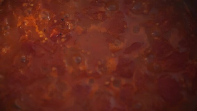 Bubbling tomato sauce in a metal pot on the stove - top view close-up. Tomato pulp and active bubbles visible. Concept of homemade pizza sauce and natural organic food preparation