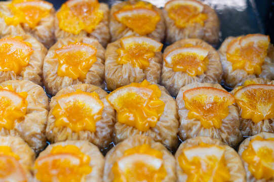 Traditional Greek orange baklava pastries soaked in syrup are topped with orange slices in Kerkira, Greece. The sweet phyllo desserts are displayed together on a tray.