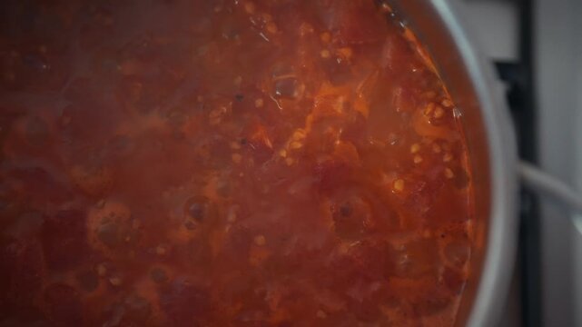 Top view close-up of tomato sauce simmering in a metal pot on the stove. Bubbles and tomato pulp visible. Concept of homemade tomato sauce preparation and cooking process