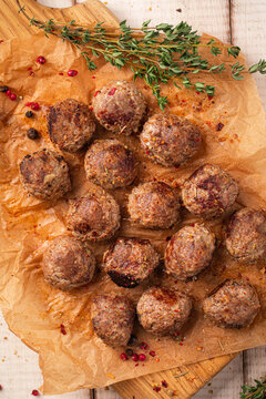 Roasted minced beef meatballs served on baking paper on wooden cutting board with spices and herbs