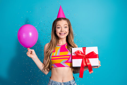 Happy young woman celebrating with balloon and gift against bright blue background, showcasing cheerful vibes
