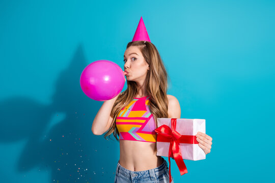 Celebratory young woman holding a festive gift box and pink balloon while enjoying a cheerful party with colorful attire