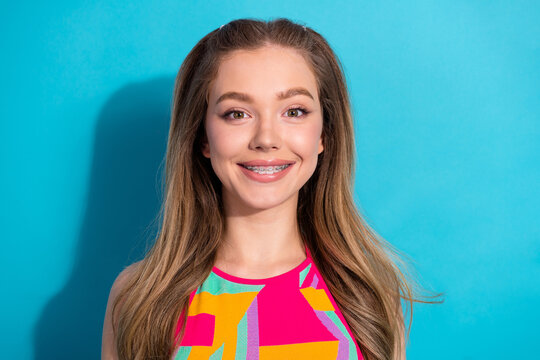 Brightly dressed girl with braces smiling confidently against a vibrant blue background, radiating youthful style and happiness