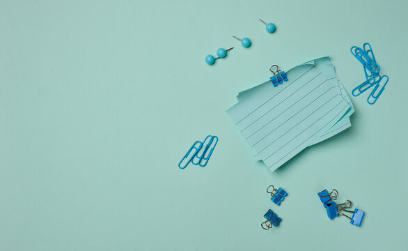 Blue stationery supplies a stack of sheets, paper clips, and pushpins on a pastel background.