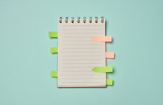 Spiral-bound lined notebook with colorful sticky index tabs on a turquoise background.