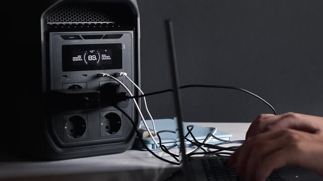 Working from home on a laptop powered by a portable power station. Concept of backup power and energy independence; energy storage, blackout, battery.
