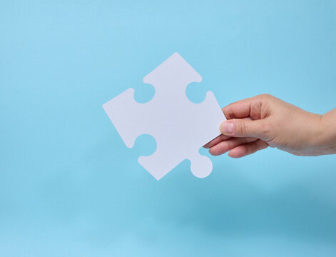 A person holding a single white puzzle piece against a blue background.