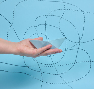 A person holding a paper boat on their palm against a background with dashed route lines.