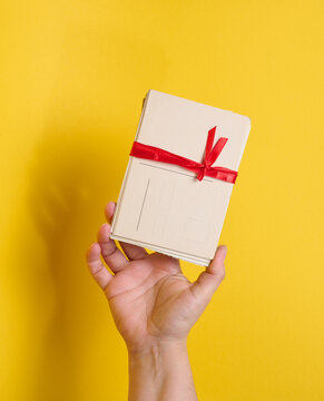 A person holding a stack of vintage postcards tied with a red ribbon and bow