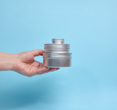 A person holding a pyramid of three round aluminum jars on their palm