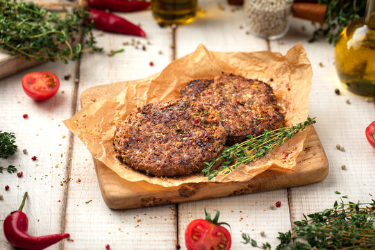Two succulent fried beef patties for burgers seasoned with herbs presented on parchment paper on rustic wooden board 