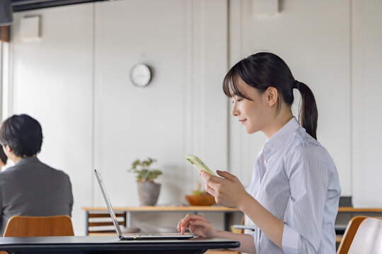 コワーキングスペースでスマートフォンとノートパソコンを使う日本人女性