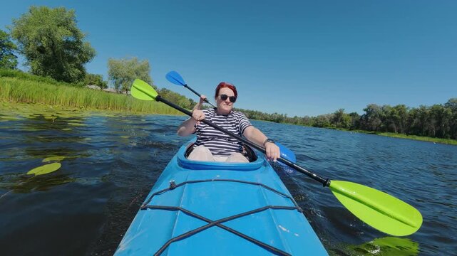 Mature woman paddling tandem kayak on calm river during outdoor summer vacation