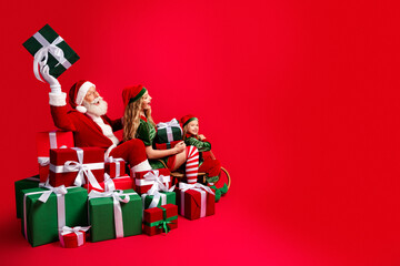 Naklejka premium Santa and two cheerful elves sitting among wrapped Christmas gifts on a vibrant red background celebrating family holiday joy and festive spirit