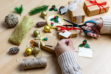 Hands preparing christmas gifts with wrapping supplies on wooden table © Marcela Ruty Romero