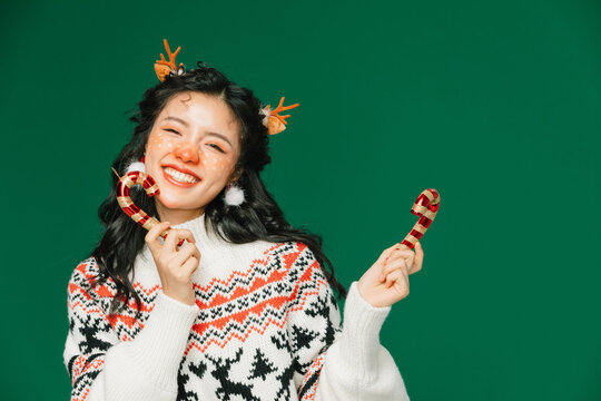 Happy young woman in Christmas sweater with reindeer antlers holding candy canes