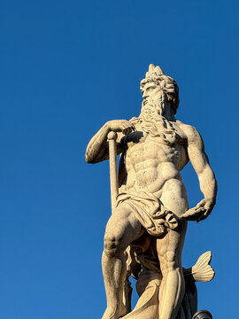 Classical marble statue of Neptune god with trident against clear blue sky