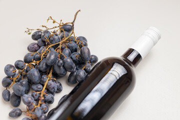 Obraz premium Dark wine bottle lying next to blue grapes on neutral background for label design and product poster