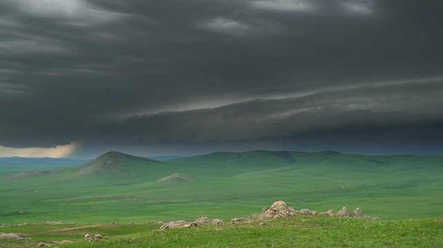 Mongolia steppe darkens under storm clouds above green plains as rain nears the horizon.