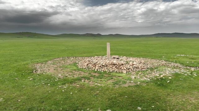 Stone kurgan and sacred stele stand on Mongolia steppe as ancient burial monument.