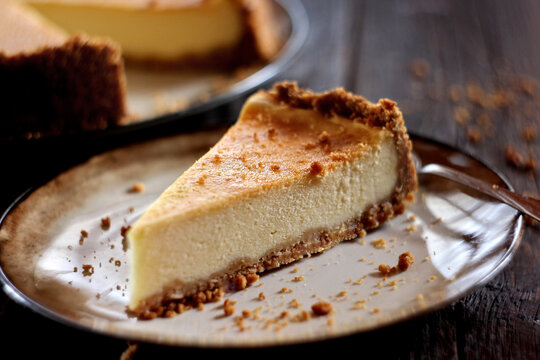 New York Cheesecake on a Rustic Wooden Background.

A slice of classic New York cheesecake with a creamy texture and graham cracker crust, served on a plate over a dark rustic wooden background. 