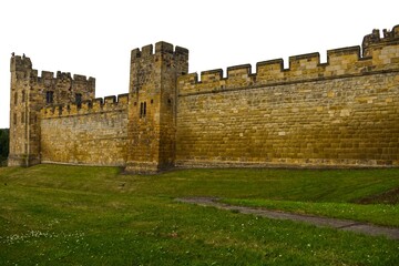 Exterior view of ancient medieval castle stone walls and towers with green grass lawn. Historic fortress defensive architecture, heritage landmark. Alnwick castle England © TomKorcak