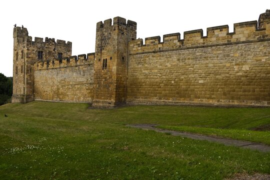 Exterior view of ancient medieval castle stone walls and towers with green grass lawn. Historic fortress defensive architecture, heritage landmark. Alnwick castle England
