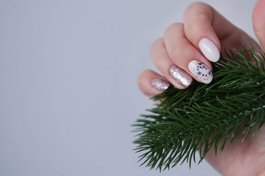 A beautiful Christmas manicure. A woman's hand holds a spruce branch, showcasing a beautiful nail design.